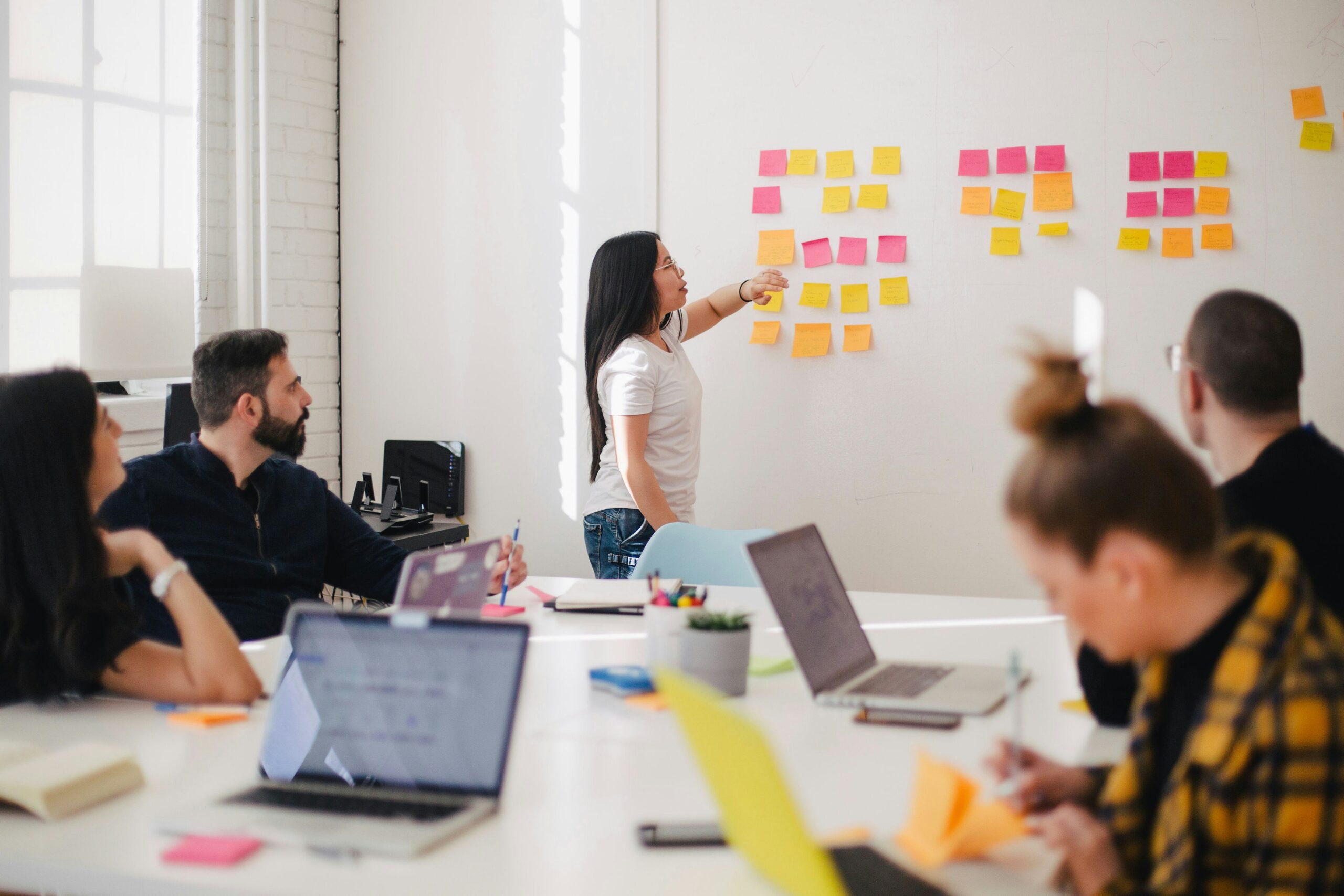 people meeting with laptops led by woman at whiteboard